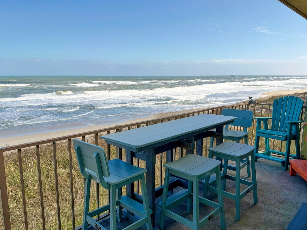 Oceanfront balcony with a high table, stools, and Adirondack chairs facing the beach and the Atlantic