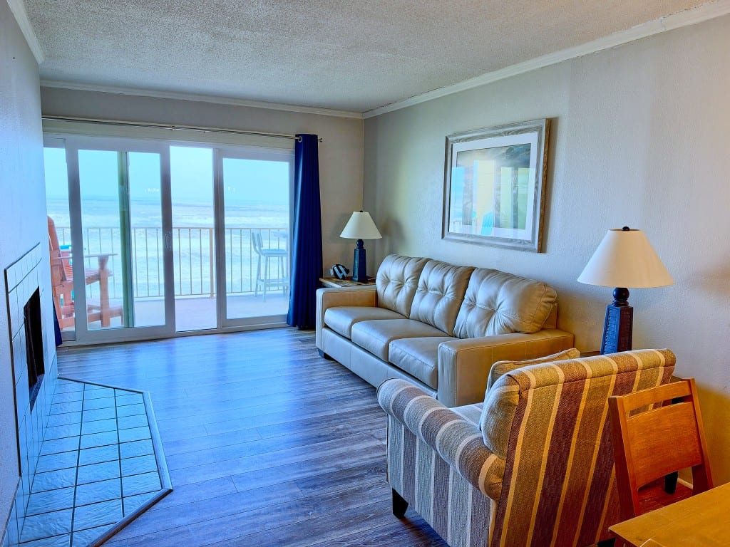 Main living room with a leather sofa, a tiled fireplace, and sliding doors to the oceanfront balcony