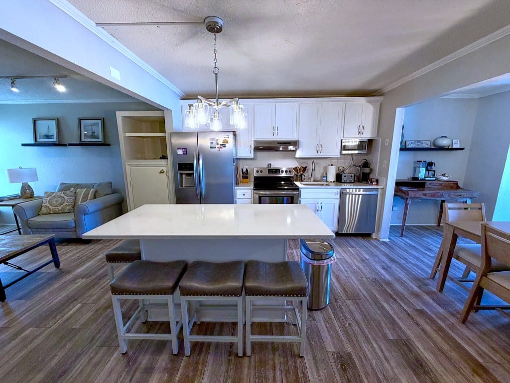 White kitchen with a stainless refrigerator, range, dishwasher, and a quartz island with four bar stools