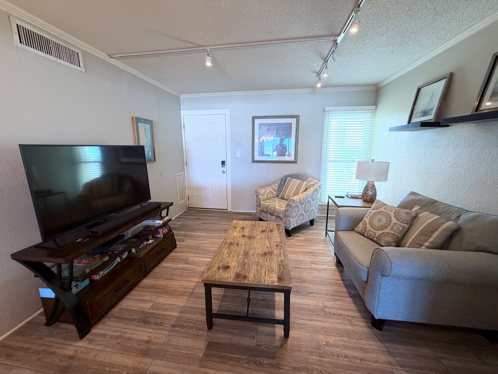 Front sitting room with a gray sofa, a patterned armchair, a wood coffee table, and a television