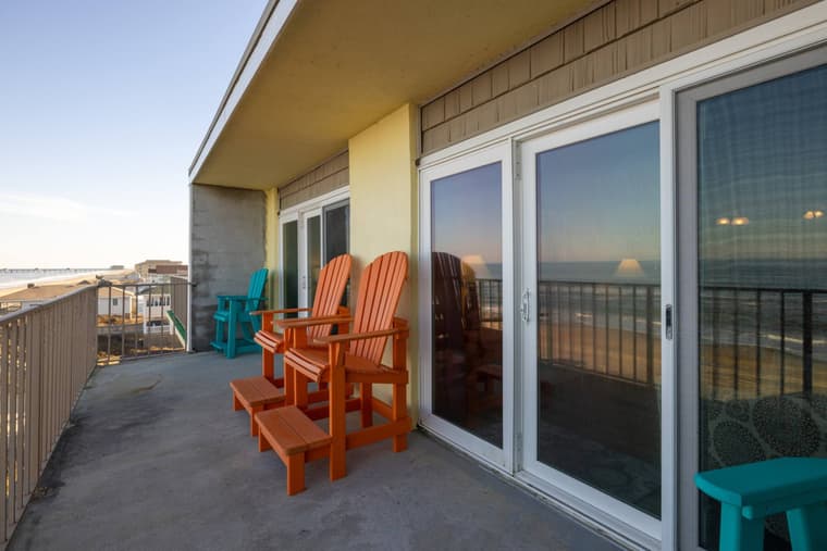 Balcony with orange and teal Adirondack chairs beside a wall of sliding glass doors.