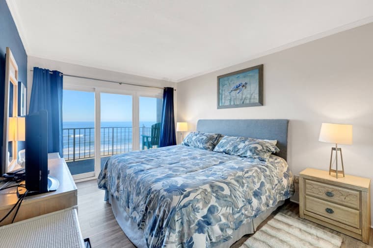Primary bedroom from the opposite corner, showing the king bed and glass doors to the balcony with the ocean beyond.