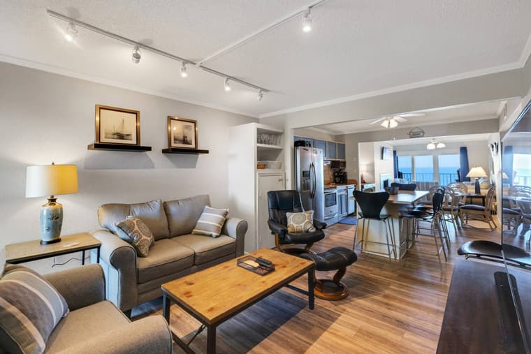 Main living room with a sofa and wooden coffee table, opening through to the kitchen and dining area with the ocean beyond.
