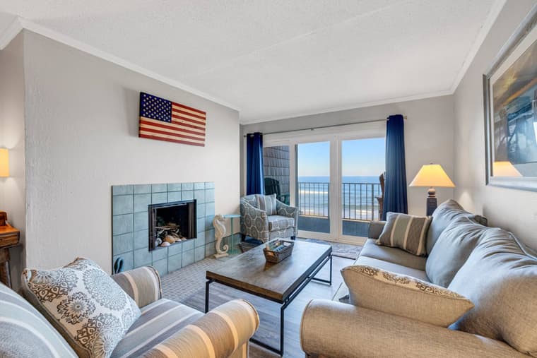 Second living room with a tiled fireplace, sofas and armchairs, and sliding doors showing the ocean.