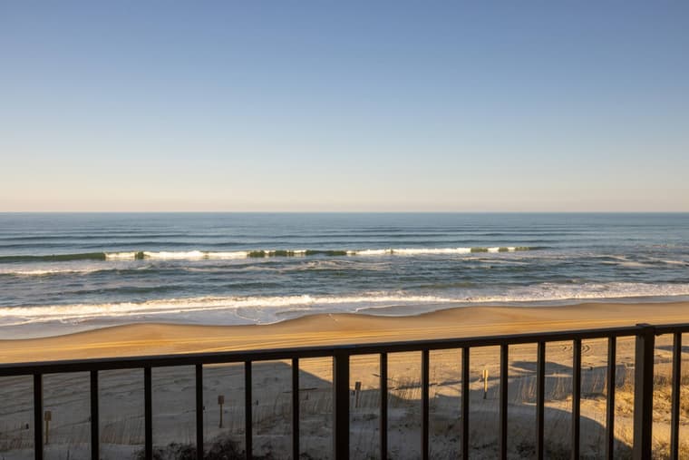View over the balcony railing to breaking waves and open beach.